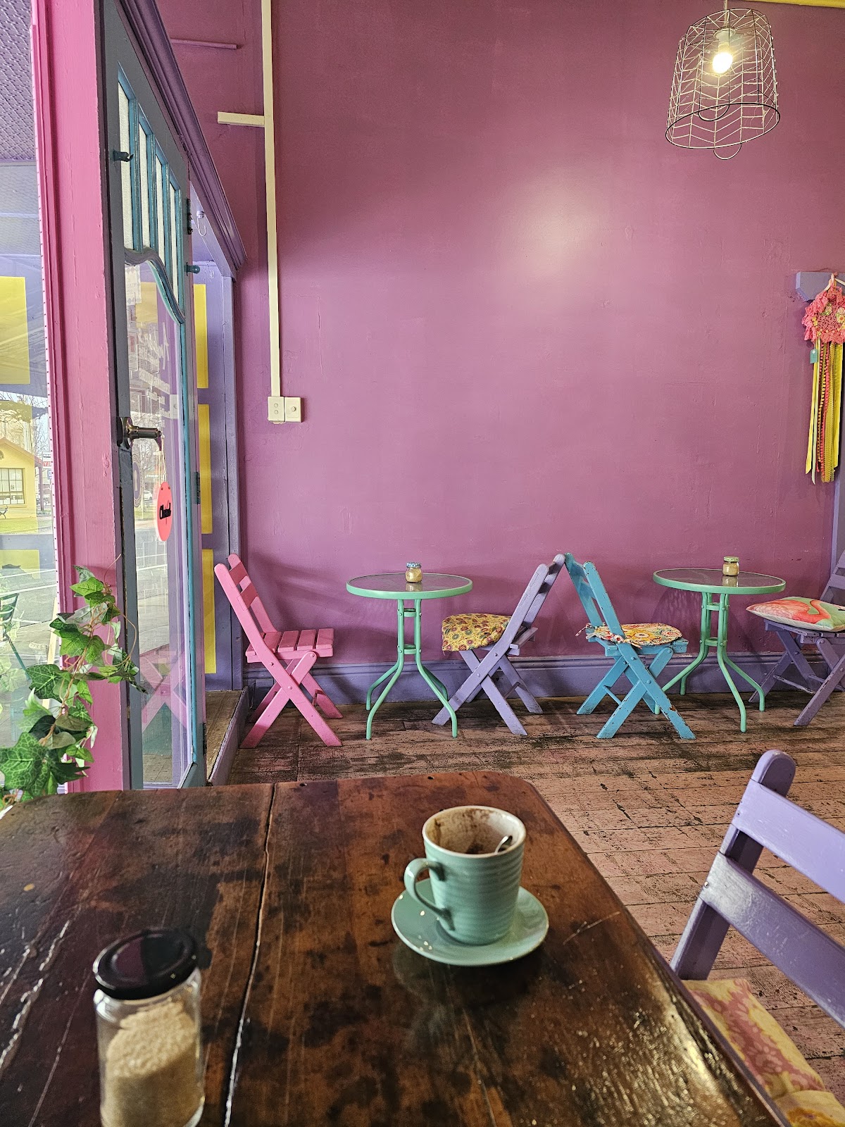 Pink walls and pastel folding chairs inside the cafe, with a coffee on a timber table