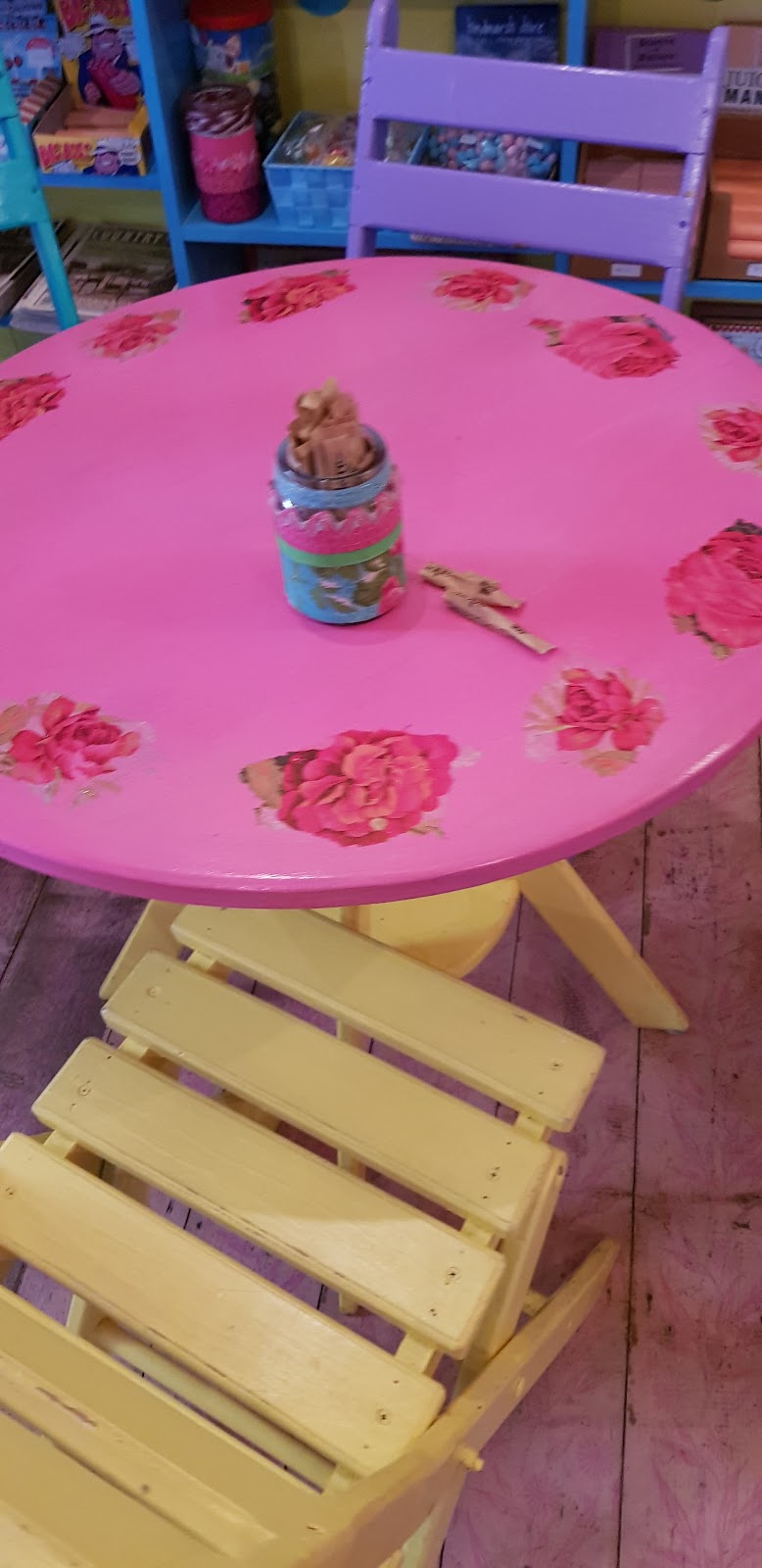 A pink table painted with roses and a yellow slatted chair